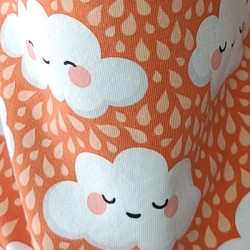 Tela estampada de nubes sonrientes sobre fondo naranja, detalle del diseño.